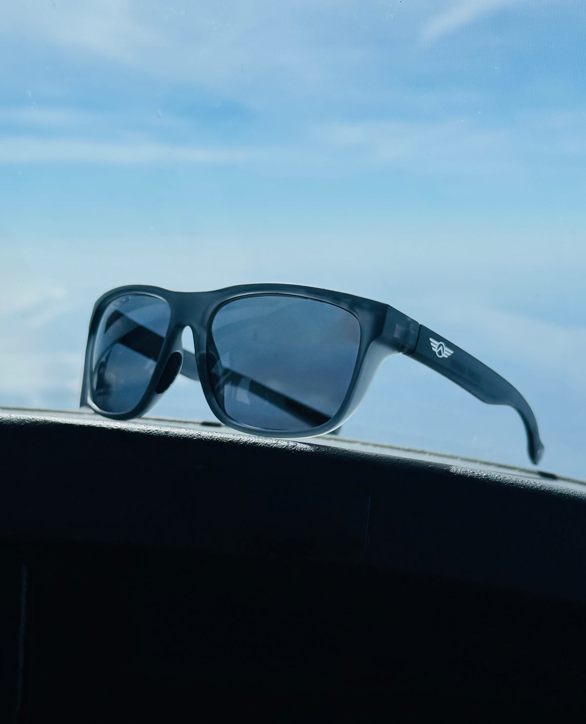 Sunglasses on a car dashboard with a clear blue sky background