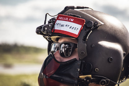 Person wearing a helmet with a 'Hello, I'm trying my best' tag on a blurred outdoor background
